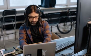 Programista z brodą w słuchawkach ANC pracuje przy laptopie w biurze